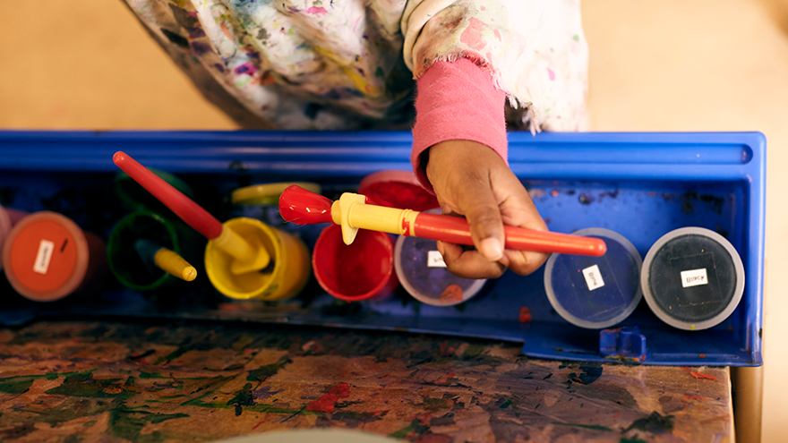 Child holding paint brush over art supplies.