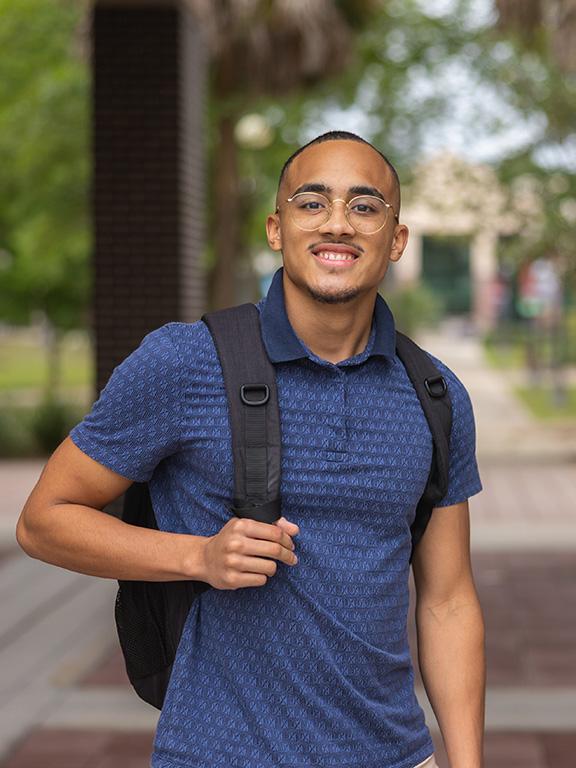 A student smiles while wearing a backpack on a Florida campus.