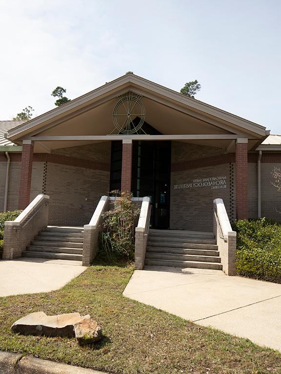 Image showing the front of the Margaret Jane Smith Archaeology Institute Building. Two sidewalks and sets of stairs lead to a entry with a peaked roof featuring a turtle medallion	